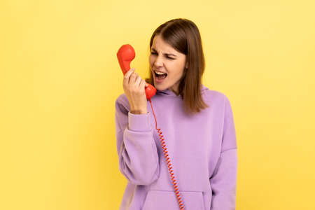 Housing maintenance call center. Angry brown haired woman shouting into retro phone handset,...
