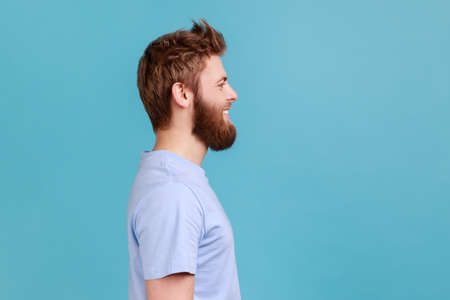 Side view of bearded man looking at camera with toothy smile and happy facial expression, being in...