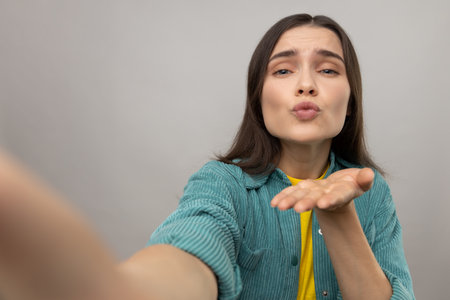 Romantic young adult woman making point of view photo, sending air kissing, POV, expressing love and...