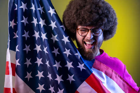 Portrait of hipster man with Afro hairstyle having fun, holding american flag, rejoicing,...