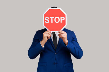 Portrait of man hiding face behind Stop symbol, red traffic sign warning of restricted access,...