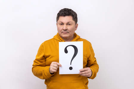 Good looking middle aged man holding question mark, finding smart solution, asking for advice, looking at camera, wearing urban style hoodie. Indoor studio shot isolated on white background.の写真素材