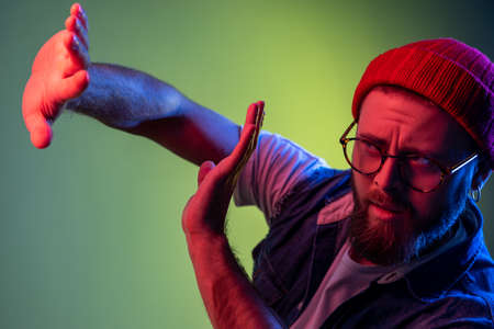 Frightened hysterical hipster man standing, raised hands to defend from fear, horrified and shocked,...
