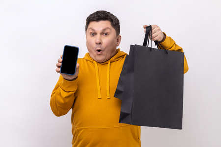 Astonished man holding cell phone and shopping bags, advertising online store on mobile device,...