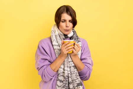 Flu treatment. Ill young woman wrapped in scarf drinking hot tea beverage, treat from seasonal...