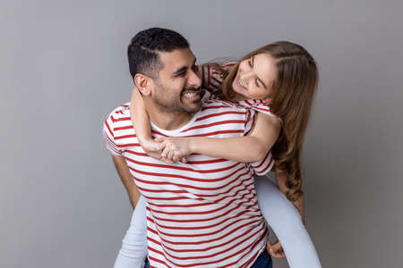Joyful father giving piggyback ride for his charming daughter, smiling girl looking at her daddy...