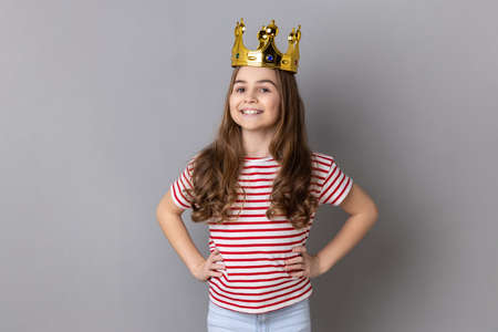 Portrait of satisfied arrogance little girl princess wearing striped T-shirt and golden diadem...