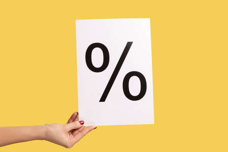 Closeup side view of woman hand holding paper with percent mark, presenting big discounts. Indoor studio shot isolated on yellow background.の写真素材