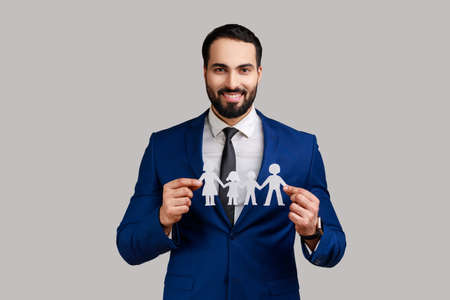 Smiling bearded man holding paper chain people in hands, concept of happy family, parenthood, childhood, wearing official style suit. Indoor studio shot isolated on gray background.の写真素材