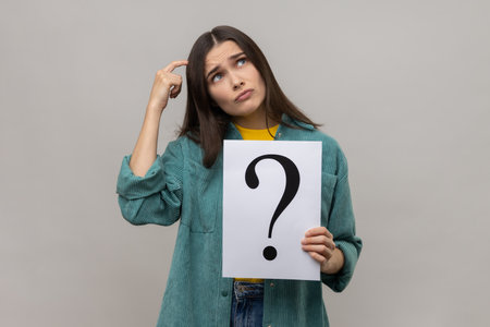 Portrait of pensive thoughtful woman looking away, holding paper with question mark, thinks about...