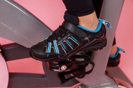 Closeup portrait of the bike simulator and womens legs in black sneakers, cardio workout. Indoor...