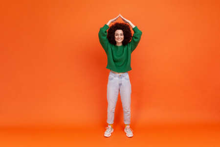Full length portrait of woman with Afro hairstyle wearing green casual style sweater holding arms...