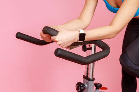 Closeup portrait of unknown woman hands with smartwatch on sport apparatus, riding exercise bike....