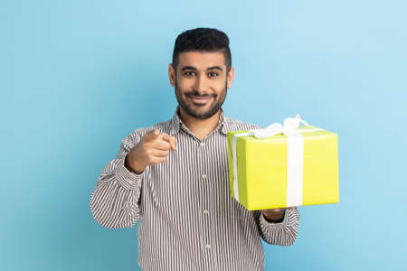 Happy bearded businessman holding gift box and pointing to camera, choosing you, showing present...