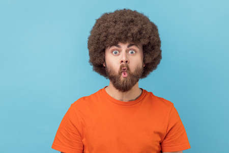 Portrait of silly man with Afro hairstyle in orange T-shirt puckers lips makes grimace, imitates...