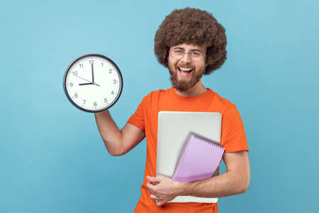 Portrait of satisfied man with Afro hairstyle wearing orange T-shirt holding paper notebook and...