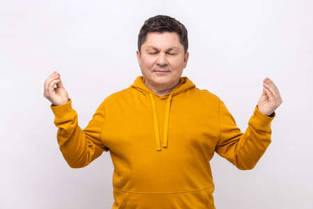 Portrait of handsome middle aged man standing with raised arms and doing yoga meditating exercise,...
