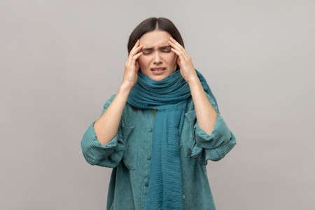 Upset frustrated woman standing wrapped in scarf, feeling headache, cold symptoms, runny nose, frowning face, wearing casual style jacket. Indoor studio shot isolated on gray background.の写真素材