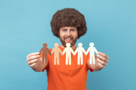 Portrait of happy man with Afro hairstyle wearing orange T-shirt holding paper people holding hands,...
