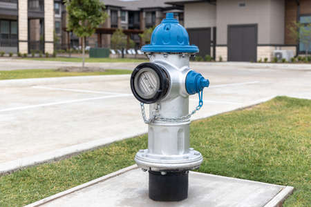 Grey and blue fire hydrant on sidewalk in the yard in residential complex with asphalt road and building on backgroundの写真素材