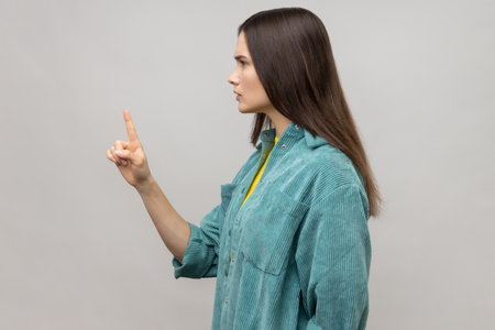 Be careful. Side view of strict bossy woman looking at camera seriously, pointing finger and warning, wearing casual style jacket. Indoor studio shot isolated on gray background.の写真素材