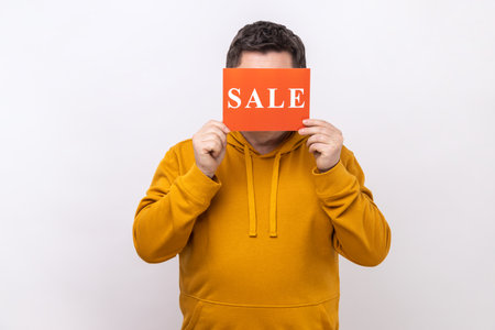 Portrait of unknown anonymous man covering eyes with Sale inscription, market discounts, black friday, wearing urban style hoodie. Indoor studio shot isolated on white background.の写真素材