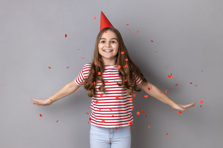 Portrait of charming extremely happy little girl wearing striped T-shirt standing with spread arms...