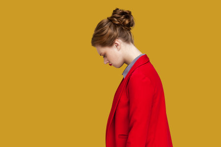 Side view portrait of worried stressed woman with red lips standing looking at camera with sad expression, feels upset, wearing red jacket. Indoor studio shot isolated on yellow background.の写真素材