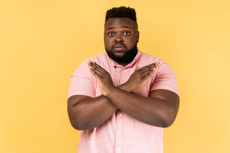 No way, absolutely not. Portrait of amazed man wearing pink shirt showing x sign with crossed hands, meaning stop, this is the end. Indoor studio shot isolated on yellow background.の写真素材