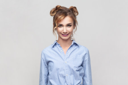 Portrait of blonde woman wearing blue shirt smiling positively after having unforgettable time with her friends, looking at camera. Indoor studio shot isolated on gray background.の写真素材