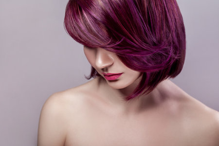 Side view portrait of calm beautiful attractive fashion model woman with short purple colored hairstyle and pink lips, looking down. Indoor studio shot isolated on gray background.の写真素材