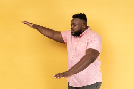 Side view of lonely blind disabled man wearing pink shirt standing with closed eyes and outstretched hands searching way, walking with doubts. Indoor studio shot isolated on yellow background.の写真素材