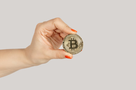 Closeup of woman hand showing golden bitcoin, cryptocurrency, virtual money. Indoor studio shot isolated on gray background.の写真素材