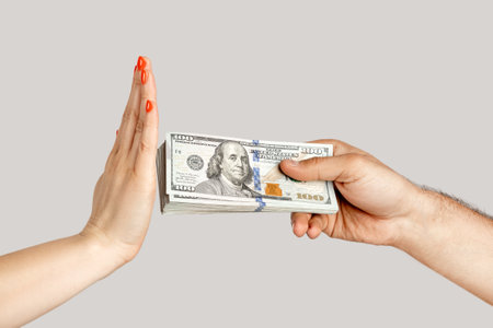 Closeup of woman hand refusing money, man hand offering dollar banknotes, corruption. showing Indoor studio shot isolated on gray background.の写真素材