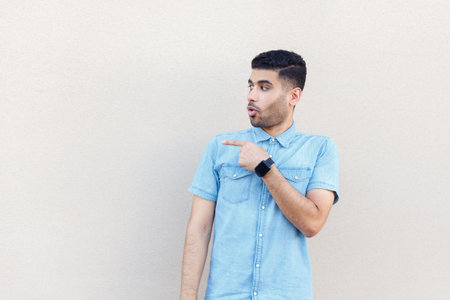 Portrait of excited astonished man wearing denim shirt looking and pointing away at advertisement area, copy space for promotion. Indoor studio shot isolated on gray background.の写真素材