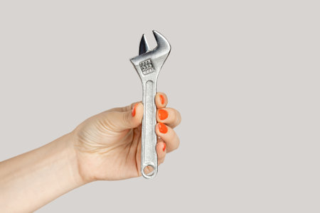 Closeup of woman hand holding adjustable wrench, mechanic and repairman tools and instruments. Indoor studio shot isolated on gray background.の写真素材