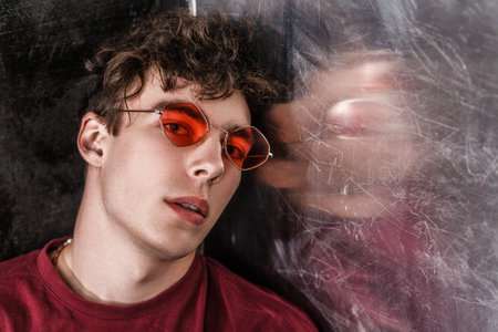 Portrait of attractive handsome fashion model man with curly hair in bright red sunglasses, wearing...