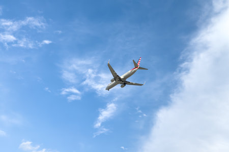 Miami, Florida - August 25th, 2023: American Airlines plane is flying in blue sky on sunny day. Travel, vacation, air transportation concept.のeditorial素材