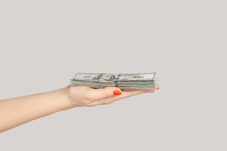 Closeup of woman hand showing dollar banknotes, earning money, salary, jackpot. Indoor studio shot isolated on gray background.の写真素材