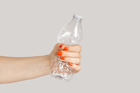 Closeup of woman hand crumpling plastic bottle, sorting rubbish, eco, saving environment. Indoor studio shot isolated on gray background.の写真素材