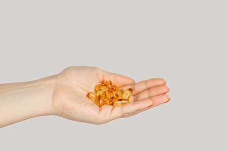 Closeup of woman hand handful of pills capsules, nutritional supplement, vitamins, medicine. Indoor studio shot isolated on gray background.の写真素材