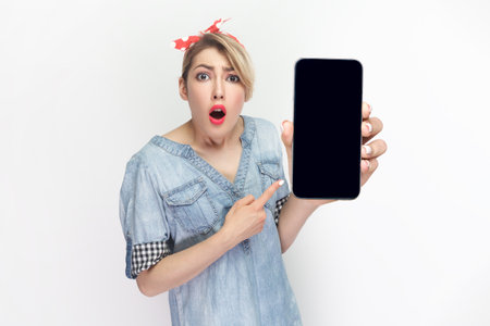 Portrait of shocked astonished blonde woman wearing blue denim shirt and red headband standing...