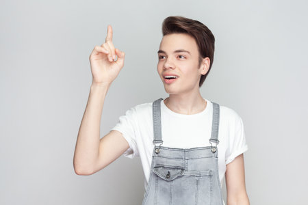 Clever man scientist get new idea of developing famous high quality kind of smart phone, raises fore finger, ready to start work on project. Indoor studio shot isolated on gray background.の写真素材