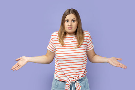 I dont know. Uncertain woman standing with confused puzzled emotion, spreading hands in questioning gesture, expressing embarrassment and doubts. Indoor studio shot isolated on purple background.の写真素材