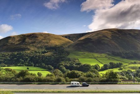 A car towing a caravan on the M6 motorway in Cumbria. The Howgill hills can be seen in the backgroundの写真素材