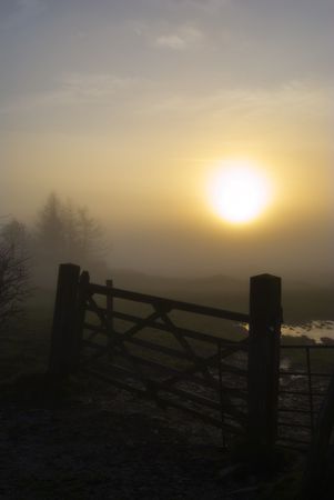 Silhouette of a wooden gate on a misty evening with the setting sunの写真素材