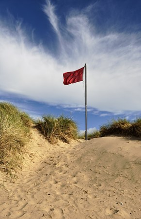 A fluttering red warning flag on a sand duneの写真素材