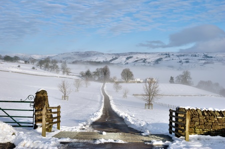 Farm track cleared of snow leading off in to the distance across snow covered fields, gate in...