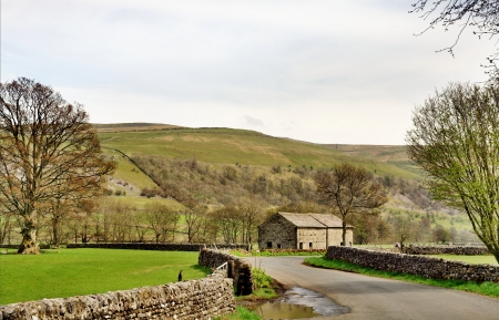 A country lane and stone built barn in the Yorkshire Dales, England, bordered by fields and set again a backdrop of fellsの写真素材