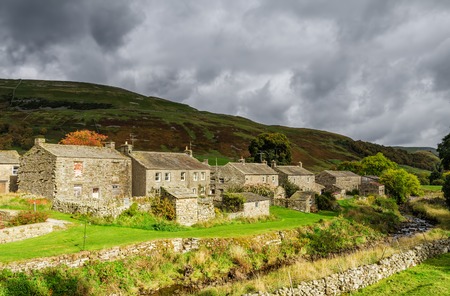Rustic stone cottages in the village of Thwaite in North Yorkshire, England on stormy overcast day with rolling green hills.の写真素材